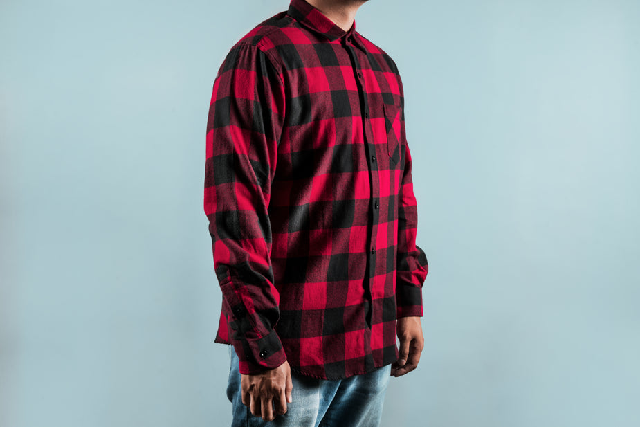 Chequered Red Shirt featuring bold buffalo plaid pattern in red and black, with long sleeves and dual chest pockets, shown against light blue background, classic flannel design with button-up front