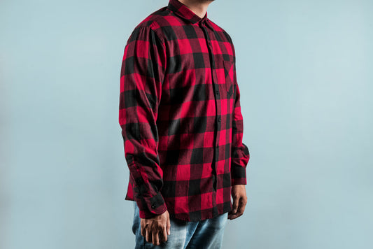 Chequered Red Shirt featuring bold buffalo plaid pattern in red and black, with long sleeves and dual chest pockets, shown against light blue background, classic flannel design with button-up front